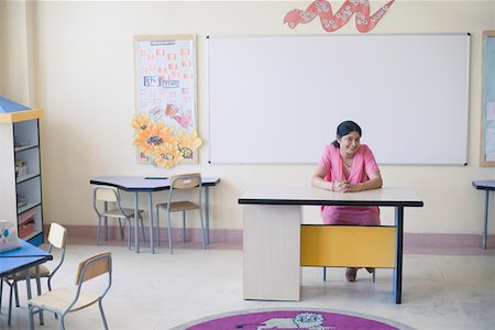 Portrait of a mid adult woman sitting at a desk and smiling in a classroom Stock Photo - Premium Royalty-Free, Code: 630-01873470