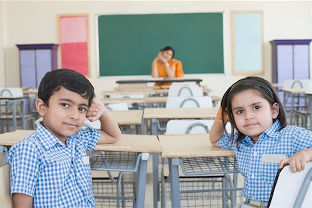 Close-up of two students sitting in a classroom with their teacher sitting in the background Foto de stock - Sin royalties Premium, Código: 630-01873587