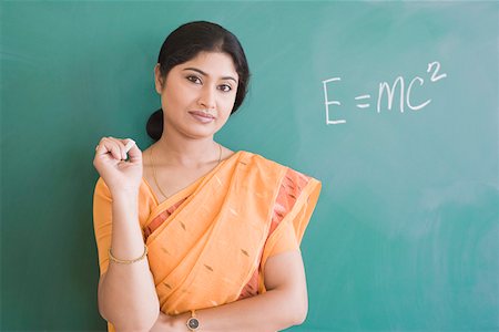 Portrait of a female teacher holding a chalk and standing in front of a blackboard Stock Photo - Premium Royalty-Free, Code: 630-01873594