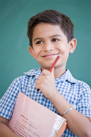 Close-up of a schoolboy holding a pencil and a book in front of a blackboard and smiling Foto de stock - Sin royalties Premium, Código: 630-01873783