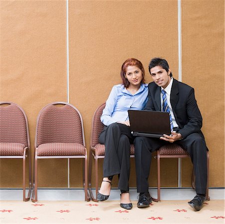 Portrait of a businessman and a businesswoman sitting on chairs with a laptop Stock Photo - Premium Royalty-Free, Code: 630-01873905