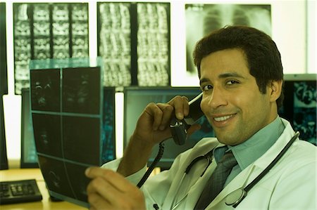 Male doctor examining an X-Ray and talking on the telephone Stock Photo - Premium Royalty-Free, Code: 630-03480734