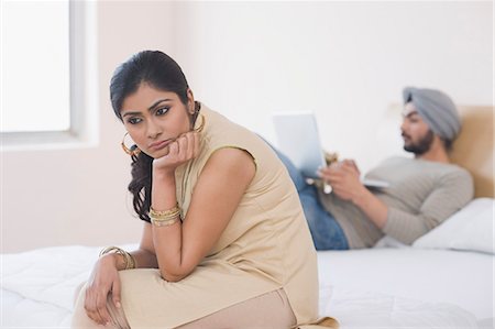 Woman looking sad while her husband working on a laptop on the bed Stock Photo - Premium Royalty-Free, Code: 630-03482786