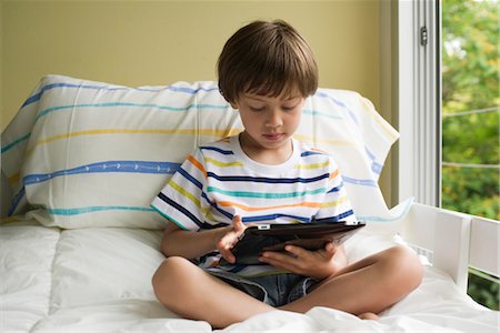 Boy sitting on bed, using digital tablet Stock Photo - Premium Royalty-Free, Code: 632-05553570