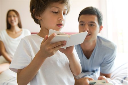 Boy reading book as parents watch in background Stock Photo - Premium Royalty-Free, Code: 632-05553895