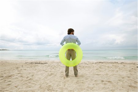 Young man staning on beach with inflatable ring, rear view Stock Photo - Premium Royalty-Free, Code: 632-05759684