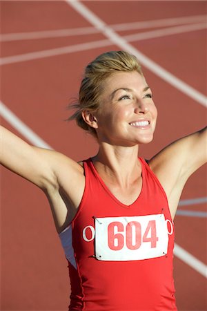 Woman running on track with arms raised in victory Stock Photo - Premium Royalty-Free, Code: 632-05760291
