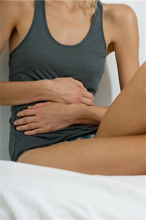 female upset stomachs - Woman sitting on bed, hands on stomach, mid section Stock Photo - Premium Royalty-Free, Code: 632-05760765