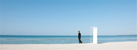 simsearch:632-03500607,k - Businessman standing on beach next to half-open door, looking at ocean Stock Photo - Premium Royalty-Free, Code: 632-05817138