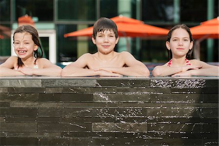 simsearch:632-06030215,k - Siblings leaning on edge of swimming pool side by side, smiling, portrait Stock Photo - Premium Royalty-Free, Code: 632-06029310