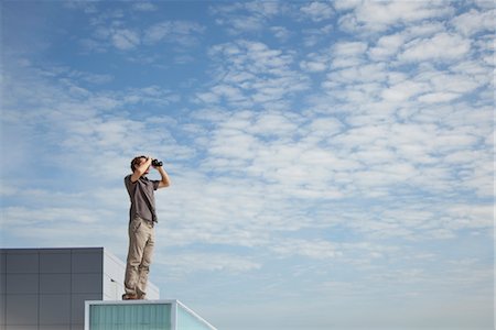 Oversized man standing on rooftop, looking through binoculars Stock Photo - Premium Royalty-Free, Code: 632-06029409