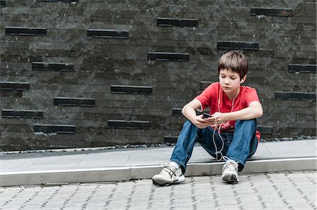 Boy sitting on sidewalk listening to music with earphones Stock Photo - Premium Royalty-Free, Code: 632-06029904