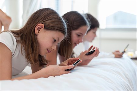 simsearch:632-03424261,k - Siblings lying on bed playing handheld video games Stock Photo - Premium Royalty-Free, Code: 632-06030090