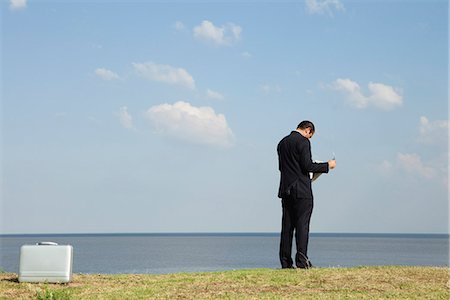 Businessman reading newspaper by ocean, rear view Stock Photo - Premium Royalty-Free, Code: 632-06118120