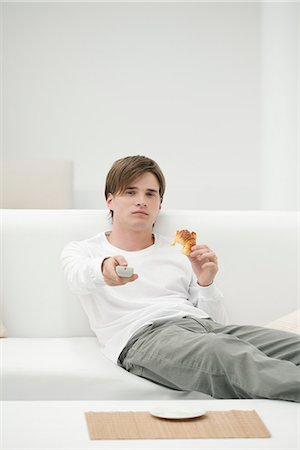 slacker - Young man eating croissant while watching TV Stock Photo - Premium Royalty-Free, Code: 632-06404236