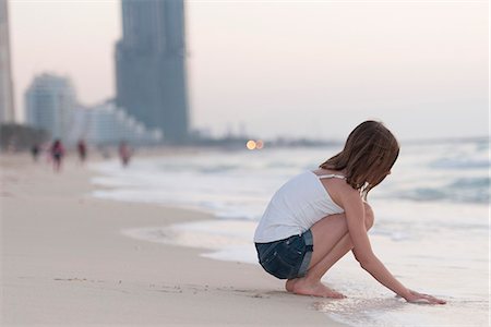 denim summer girl - Girl crouching on beach playing with water, side view Stock Photo - Premium Royalty-Free, Code: 632-07161468