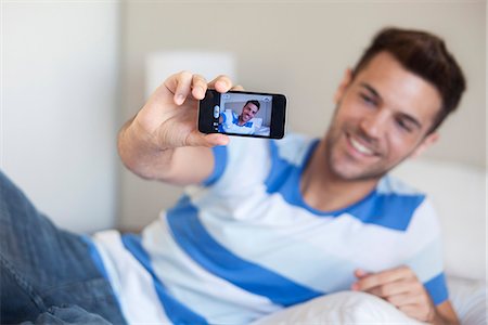 Young man reclining on bed taking selfie with smartphone Stock Photo - Premium Royalty-Free, Code: 632-07674531