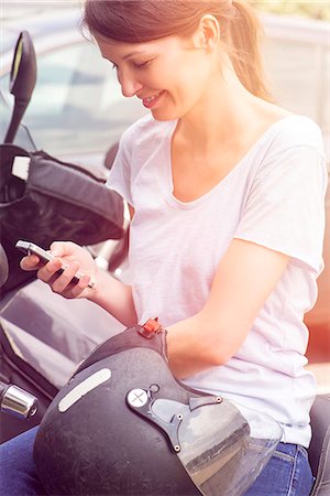 simsearch:632-05760692,k - Woman sitting on motorcycle, smiling at smartphone Stock Photo - Premium Royalty-Free, Code: 632-08130220