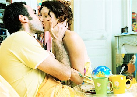 Man in bed with breakfast tray on lap, kissing woman, side view. Stock Photo - Premium Royalty-Free, Code: 632-01144066