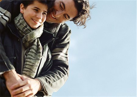 protector - Adult man with arms around boy from behind, both in warm clothes, portrait, close up, sky in background Stock Photo - Premium Royalty-Free, Code: 632-01148477