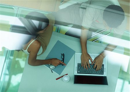 Man working on laptop, woman sitting on table pointing at laptop, through glass, high angle view Stock Photo - Premium Royalty-Free, Code: 632-01149996