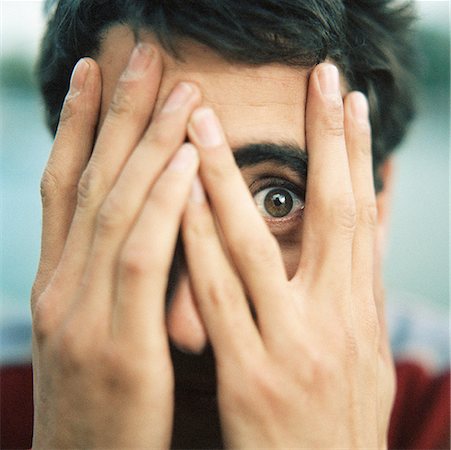 petrified (terrified) - Young man with hands over face, looking through fingers with one eye, close-up Stock Photo - Premium Royalty-Free, Code: 632-01141129