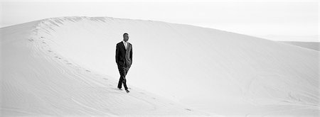 simsearch:695-03386286,k - Businessman walking across ridge of dune with hands in pocket, b&w, panoramic view Stock Photo - Premium Royalty-Free, Code: 632-01143354
