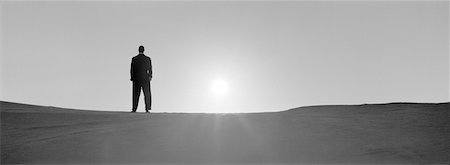 future of the desert - Man standing on sand, backlit by sun, b&w, panoramic view Stock Photo - Premium Royalty-Free, Code: 632-01143351