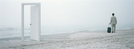 Man walking with suitcase on beach in mid-distance, doorframe in foreground Stock Photo - Premium Royalty-Free, Code: 632-01156100