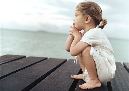 Girl crouching on dock, sea in background Stock Photo - Premium Royalty-Free, Code: 632-01150344