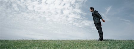 Man in suit standing on grass leaning forward with arms lifted backwards, side view Stock Photo - Premium Royalty-Free, Code: 632-01151396