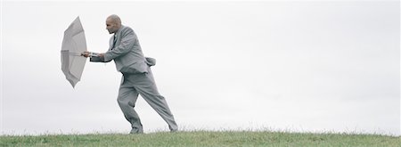 Man walking into wind with open umbrella shielding him, full length Stock Photo - Premium Royalty-Free, Code: 632-01151403