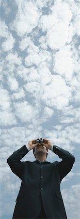 Man looking through binoculars, sky in background, low angle view Stock Photo - Premium Royalty-Free, Code: 632-01151432
