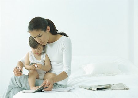 simsearch:632-03027302,k - Woman sitting on edge of bed with little girl on lap, looking down at agenda Stock Photo - Premium Royalty-Free, Code: 632-01151500