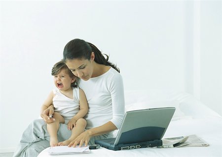 Woman sitting on bed with little girl on lap crying, looking down at paper Stock Photo - Premium Royalty-Free, Code: 632-01151501