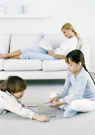 simsearch:632-03424261,k - Girl and boy playing cards on floor, woman sitting on sofa reading in background Stock Photo - Premium Royalty-Free, Code: 632-01151539