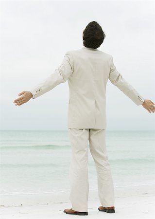 Businessman standing on beach with arms out, rear view Stock Photo - Premium Royalty-Free, Code: 632-01160285