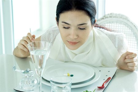 eating disorder - Woman sitting at set table, wearing napkin around neck, vitamins on plate Stock Photo - Premium Royalty-Free, Code: 632-01277040