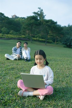 simsearch:614-06442812,k - Girl sitting in grass using laptop, parents sitting in background Stock Photo - Premium Royalty-Free, Code: 632-01270894