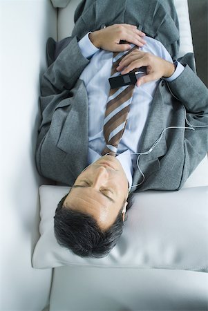 Businessman lying down, listening to earphones Stock Photo - Premium Royalty-Free, Code: 632-01271138