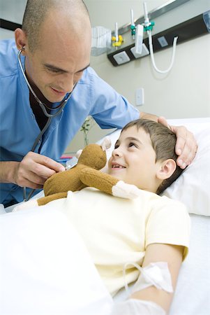 doctor intern male white - Boy lying in hospital bed, intern holding stethoscope to boy's stuffed animal Stock Photo - Premium Royalty-Free, Code: 632-01380289