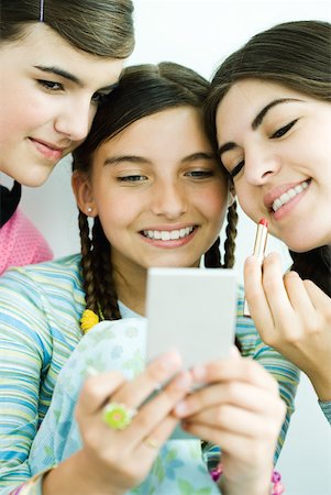 Three young female friends looking at selves in hand mirror, one holding lipgloss Stock Photo - Premium Royalty-Free, Code: 632-01380451