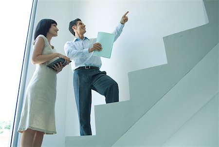 staircase arrow - Businessman and young businesswoman standing on stairs, looking up, pointing Stock Photo - Premium Royalty-Free, Code: 632-01613120