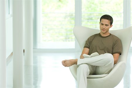 Young man sitting in chair reading book Stock Photo - Premium Royalty-Free, Code: 632-01785171