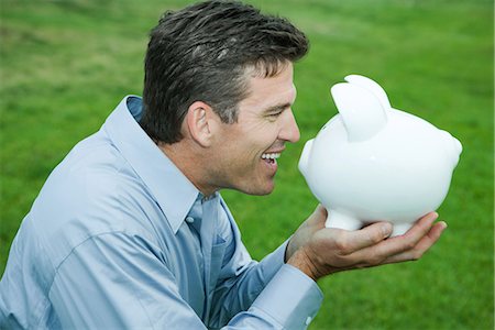 piggy - Man holding up piggy bank to face, smiling, side view Stock Photo - Premium Royalty-Free, Code: 632-01785531