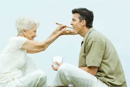 Senior woman feeding adult son takeout food with chopsticks, side view Stock Photo - Premium Royalty-Free, Code: 632-01828395