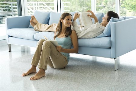 Young man lying on couch reading book, girlfriend sitting on the ground next to him Stock Photo - Premium Royalty-Free, Code: 632-01828499