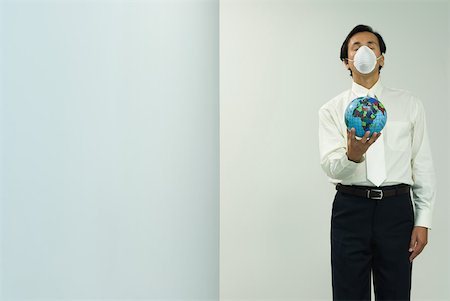Businessman wearing pollution mask, holding out globe, eyes closed, front view Stock Photo - Premium Royalty-Free, Code: 632-01828556