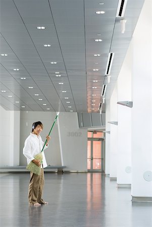 Man standing in lobby, playing air guitar with broom, listening to headphones, smiling at camera Stock Photo - Premium Royalty-Free, Code: 632-02128197