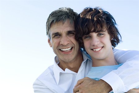 Father hugging his son from behind, smiling at camera, portrait Stock Photo - Premium Royalty-Free, Code: 632-02128268